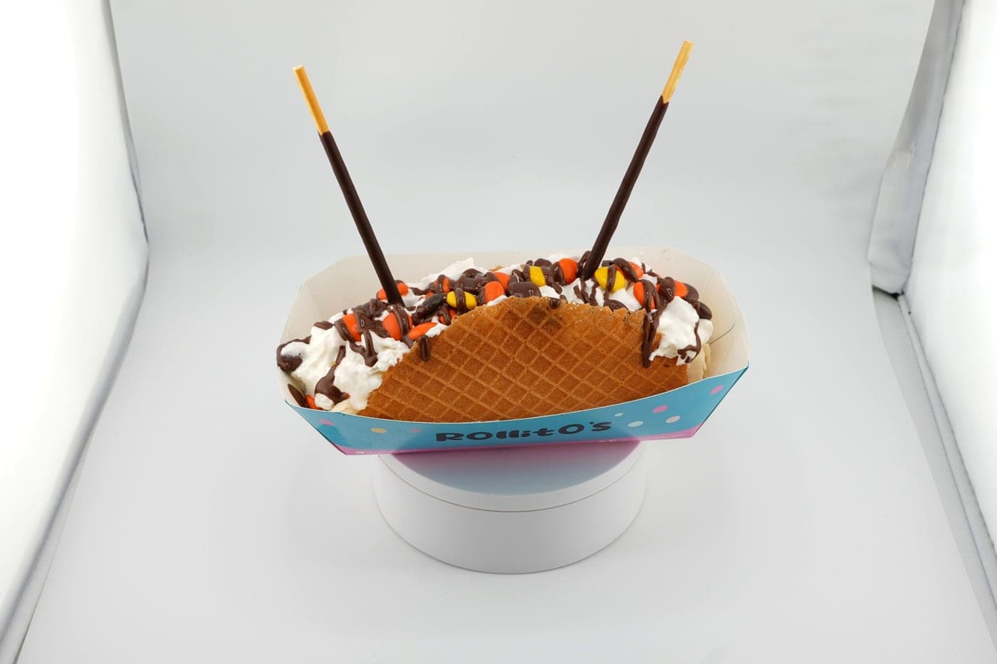 Golden waffle taco roll with whipped cream, peanut butter candies, chocolate drizzle, and Pocky sticks